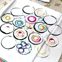 Sheet of paper with colorful stamped circles in black, pink, yellow, and blue paint.