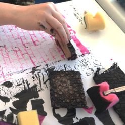 person stamping pink paint with textured materials during a printmaking activity.