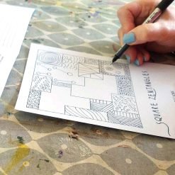 Person with light blue nail polish drawing patterns in square sections on a 'Square Zentangles' sheet.