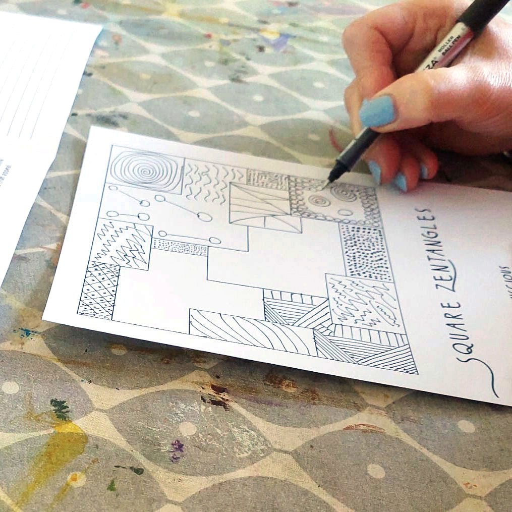 Person with light blue nail polish drawing patterns in square sections on a 'Square Zentangles' sheet.