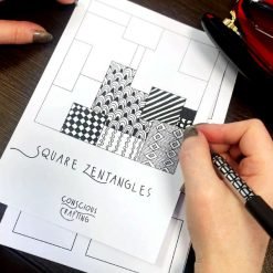 erson drawing black-and-white patterns in square sections on a 'Square Zentangles' template from Conscious Crafting.