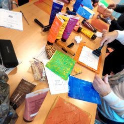 Group using rollers and acrylic paints to print colorful designs and text during a creative workshop.