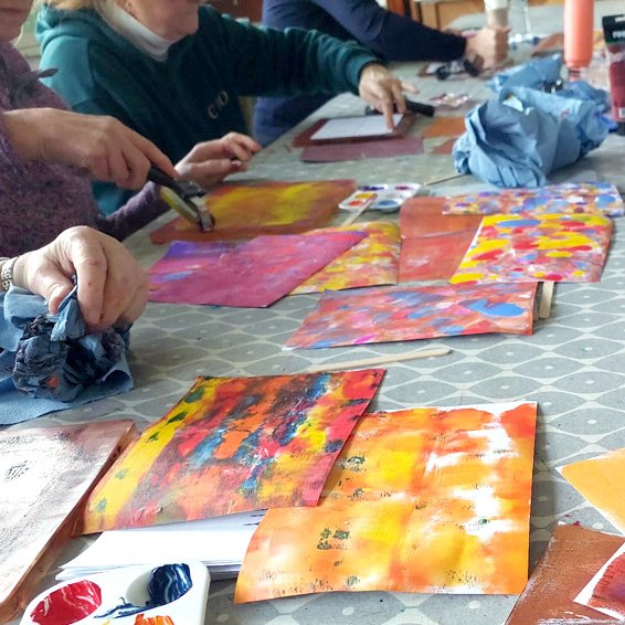 Group painting colorful abstract artworks at a table filled with brushes, palettes, and paper towels.