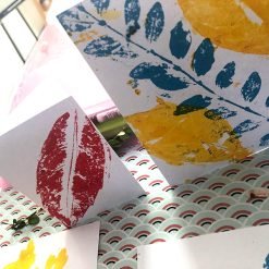 Handmade cards with colorful leaf prints in blue, yellow, and red on a patterned background.