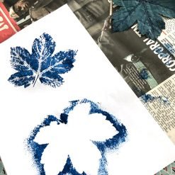 Two blue leaf prints on white paper, one detailed and one silhouetted, with a painted leaf nearby.