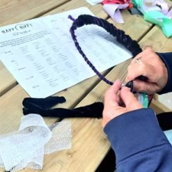 Person wrapping colorful fabric strips around a circular base while following 'Happy Hippie Headbands' instructions.
