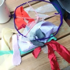 Handmade hoop wrapped in purple yarn with colorful ribbons tied to it, placed on a wooden surface.