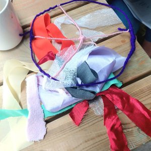 Handmade hoop wrapped in purple yarn with colorful ribbons tied to it, placed on a wooden surface.