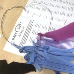 A tangled bundle of fabric scraps in light blue, dark brown, and bright red, with a thin wire loop around them, placed on a dark blue surface.