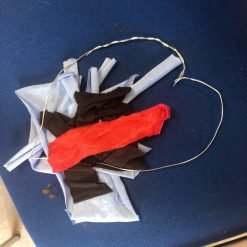 A tangled bundle of fabric scraps in light blue, dark brown, and bright red, with a thin wire loop around them, placed on a dark blue surface.