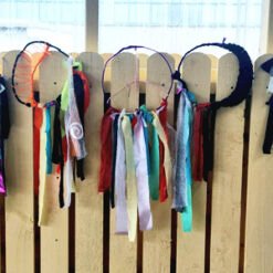 A row of colorful fabric tassels hanging from circular frames on a wooden fence.