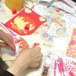 Person assembling colorful paper cutouts on greeting cards using glue and printed templates.