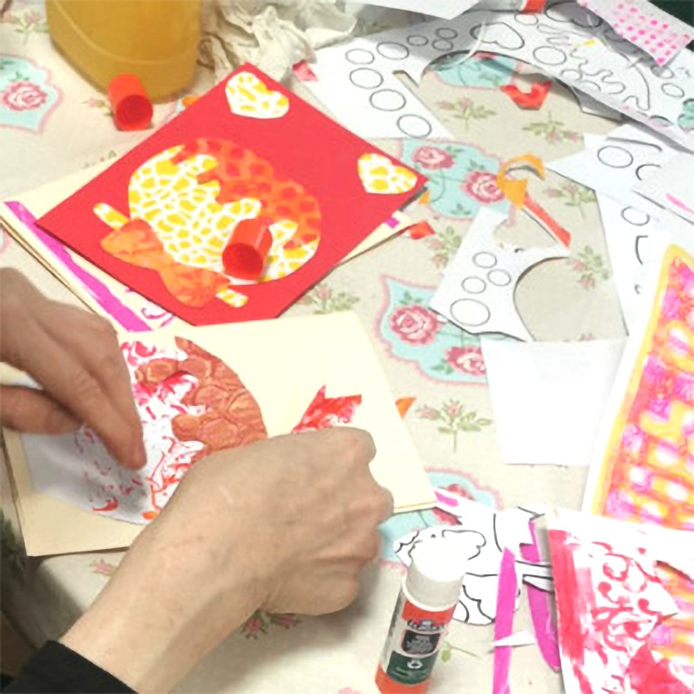 Person assembling colorful paper cutouts on greeting cards using glue and printed templates.
