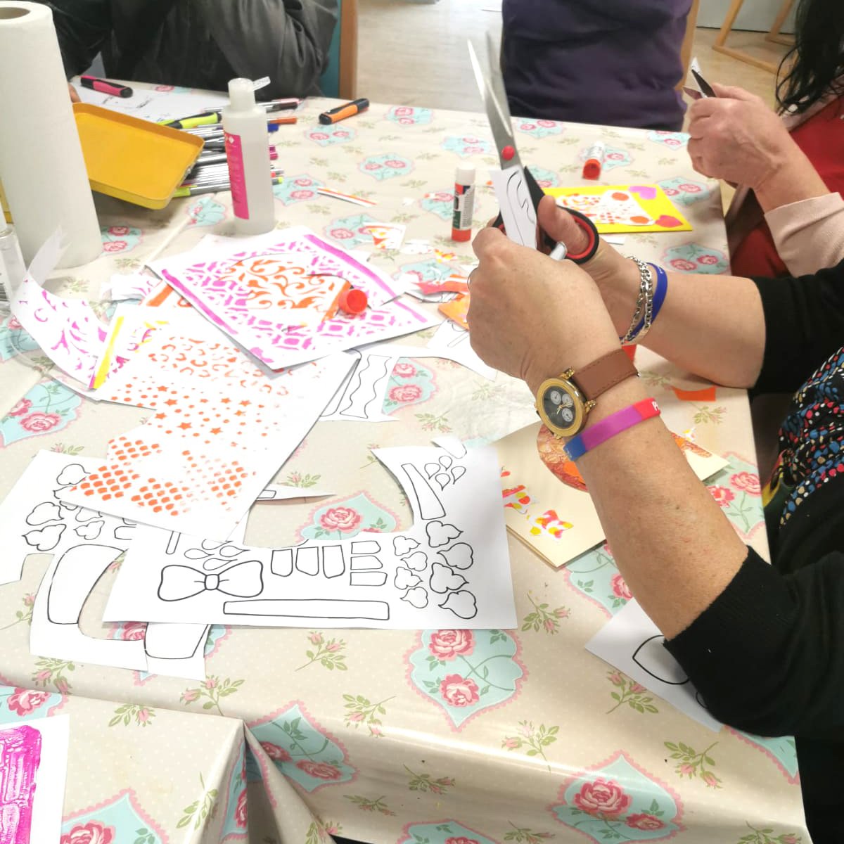 Group crafting at a table with scissors, glue, and patterned paper cutouts.