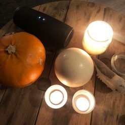 Wooden table with pumpkin, ostrich egg, lit candles, speaker, and carved fish in warm candlelight.