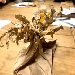 Brown paper sculpture shaped like a tree with twisted branches on table surrounded by craft materials.