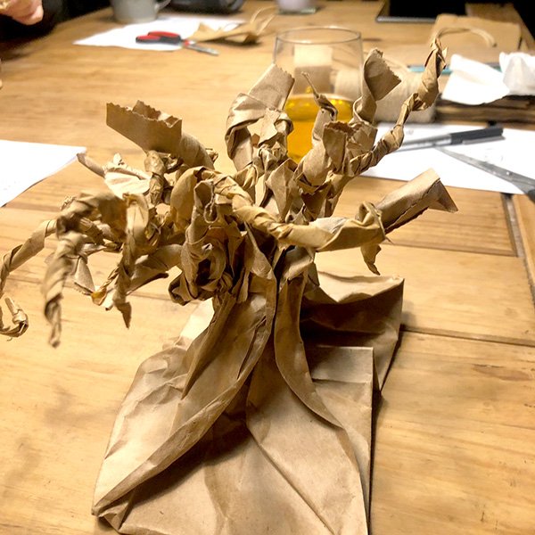 Brown paper sculpture shaped like a tree with twisted branches on table surrounded by craft materials.