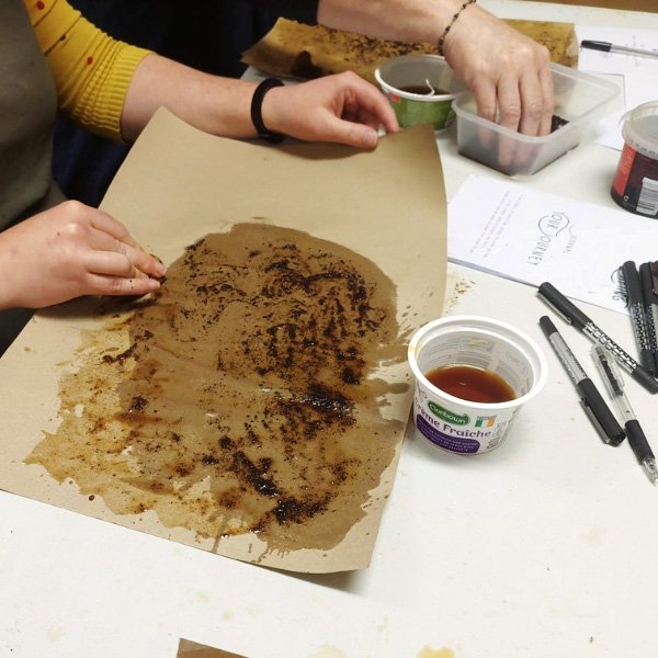 Hands working with stained paper and coffee grounds beside containers and a 'Crème Fraîche' cup.