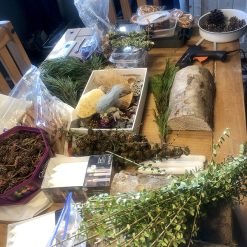 Wooden table with pinecones, dried flowers, candles, glue gun, and natural materials for crafting.