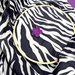 Embroidery hoop holding zebra-print fabric with purple felt flower and two needles inserted.