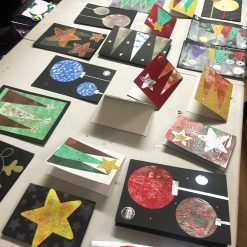 Handmade holiday cards with stars, trees, and ornaments crafted from glitter, foil, and colored paper.