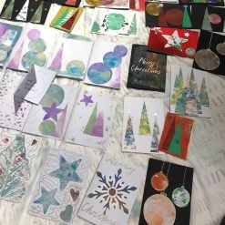 Handmade holiday cards with Christmas trees, ornaments, and stars arranged on satin surface.